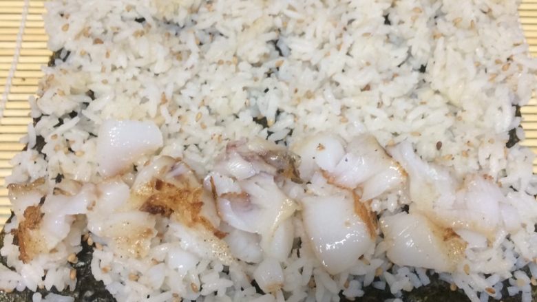 鳕鱼肉松寿司,把拌好的米饭铺在海苔上铺平，最好用勺子轻轻压一下，最下边一头放入一排鱼肉块