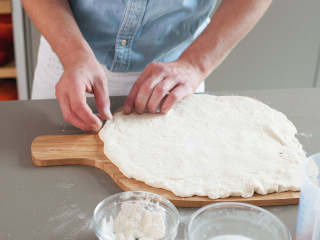 拿波里披萨,将面团拿出碗外。在撒好面粉的工作台上，压平到与披萨板差不多大小，然后放到披萨铲中。