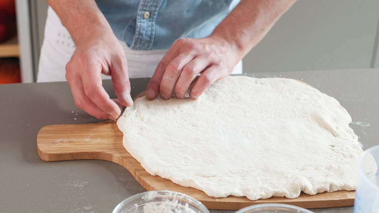 拿波里披萨,将面团拿出碗外。在撒好面粉的工作台上，压平到与披萨板差不多大小，然后放到披萨铲中。