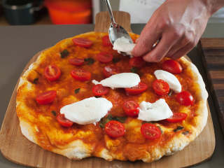 拿波里披萨,与此同时，将樱桃番茄切半，水牛奶酪切成薄片。将披萨从烤箱中取出；将番茄和奶酪放在披萨上后，再将其放回烤箱，烤上6-7分钟，直至芝士融化，而面皮变得金黄。