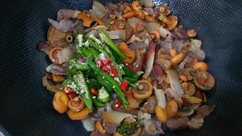 野松菌烧腊肉,汤汁明显减少后加入土青椒和红米椒，加入盐，翻炒三分钟