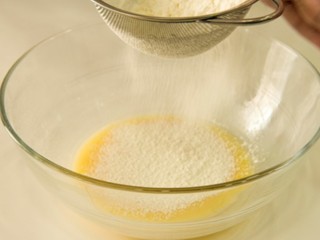 柠檬戚风小蛋糕,将事前混合好的低筋面粉、玉米粉过筛加入。过筛可令成品蛋糕的口感更加细腻