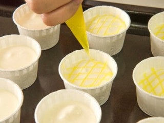 柠檬戚风小蛋糕,再取少量的柠檬酱也同时放入裱花袋里，剪小空，依次在蛋糕糊的表面画出网状纹路。这里剪的孔不要太大，避免画出来的线条过于粗糙不细致