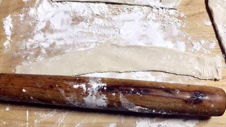 苹果玫瑰酥,案板上撒面粉，把以前冰箱里拿出室温回温的飞饼切成大概3到4厘米宽的长条，用擀面杖再擀宽一点。