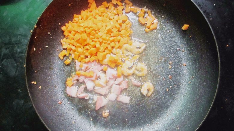 台式凤梨饭,锅底少许油然后倒入胡萝卜丁、虾仁、培根丁翻炒片刻。