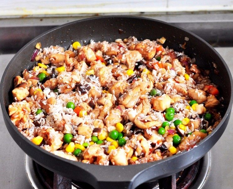 什锦鸡肉饭,倒入淘洗干净的米和蔬菜（玉米、青豆、胡萝卜），稍微翻炒均匀。