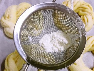 孜然芝麻花环面包,二次发酵完成后，预热烤箱180度
用一个小漏勺舀取一点面粉，筛在每个小花环面包上
表面也可以刷蛋液，在揉面团时预留一点蛋液即可
