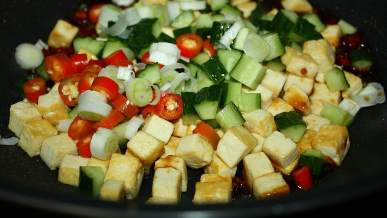 美味下饭宫保豆腐,豆腐丁、黄瓜丁、葱段和红椒圈依次入锅，快速翻炒均匀。