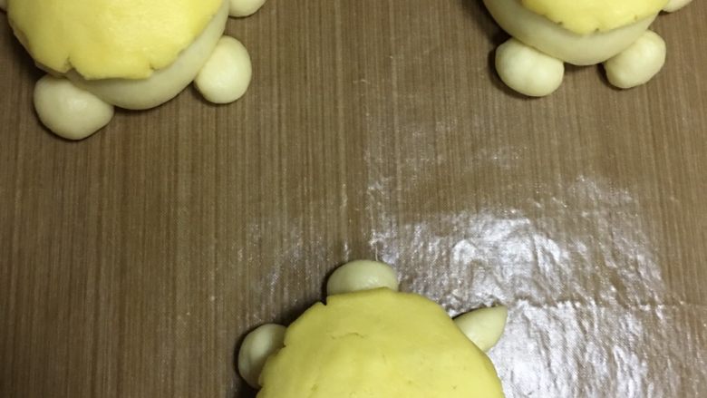 萌小龟面包,把冷藏过的酥皮取出，平均分成八份，用几个取几个搓圆，压扁盖在乌龟背上，进行二次发酵，发酵时要放热水