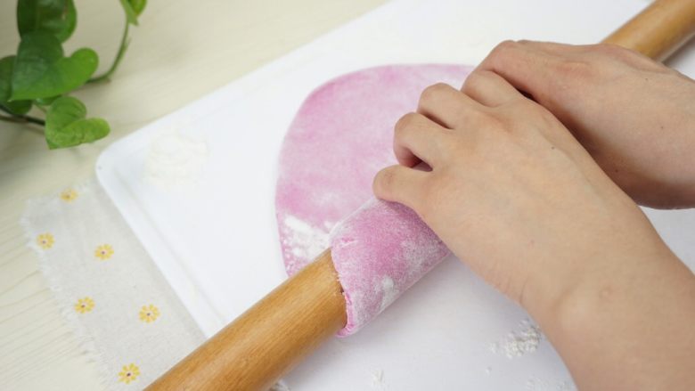 手工面,稍微大一点后，在面皮上面撒一层干面粉，用擀面杖卷起面饼的一端。