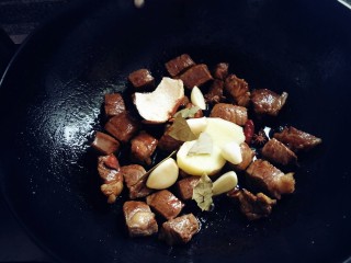 红烧牛肉炖土豆,放入姜片蒜片炒均匀。