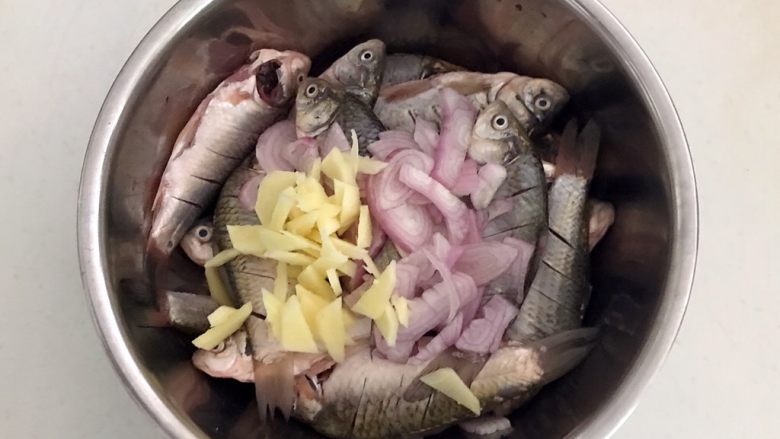 干炸鲫鱼,把圆葱片和姜片放入鱼盆里面
