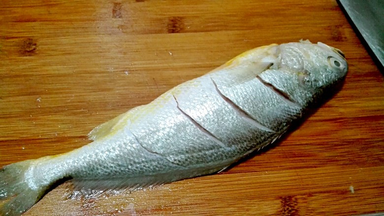 披红戴绿的蒜香红辣椒蒸黄鱼,冲洗干净，用刀在鱼背上面划几刀