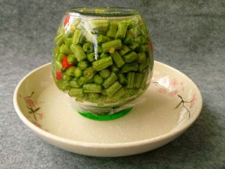 #酸味#自制酸豆角,如图，把装有长豆角的玻璃罐倒放在装有水的碗中，水能腌过瓶盖即可。