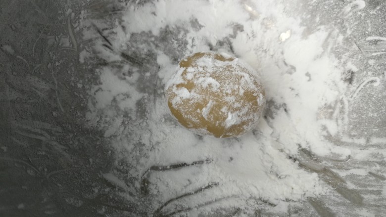 广式莲蓉蛋黄月饼,盆子里倒入玉米淀粉做手粉防粘，包好的月饼团成椭圆形放入玉米淀粉里滚一圈，轻轻拍去多余的粉