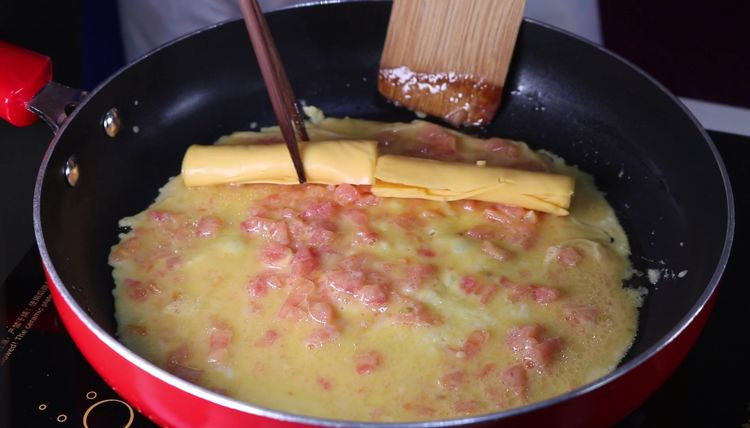 最普通的西红柿炒鸡蛋，这样吃瞬间变高大上,小火满煎至蛋液底部凝固后，将芝士卷放在蛋液上。