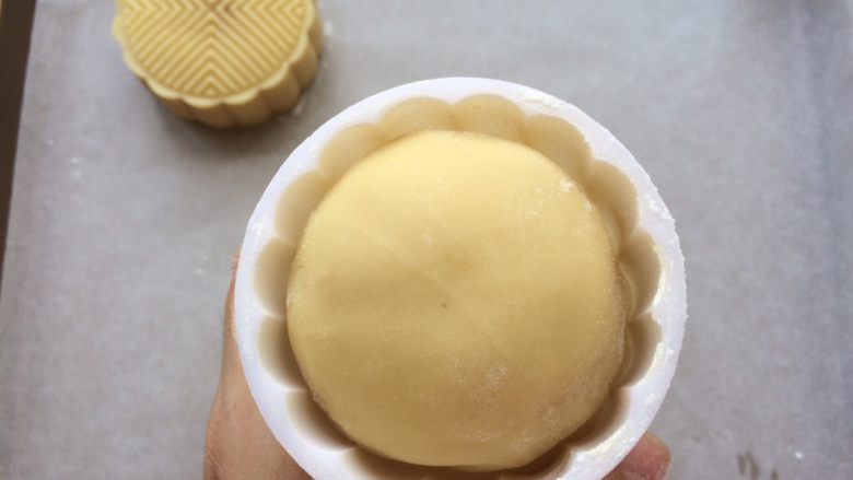 广式冰皮蛋黄月饼,模具撒入适量的低粉，抖掉多余的粉，月饼团放入模具中轻轻用手中按压一下底部。