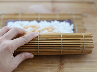 金枪鱼寿司,将竹帘慢慢卷起来，把所有食材包裹进去，在收口处的紫菜上刷一层清水，这样粘的比较牢固