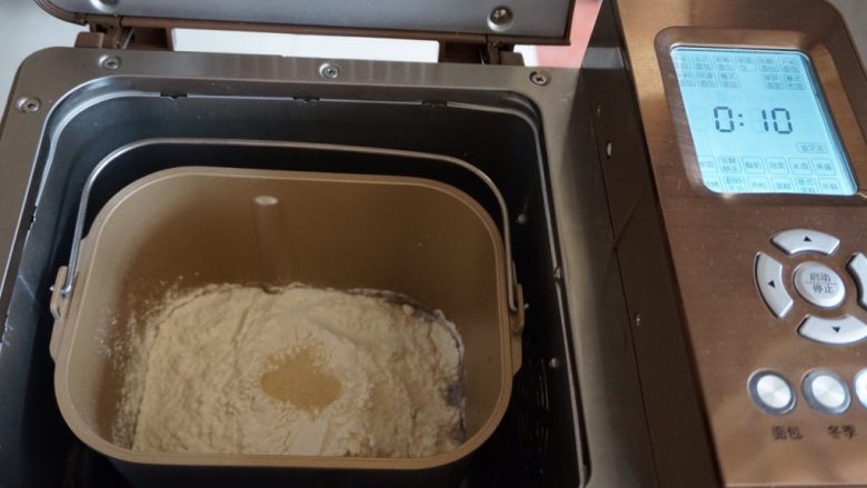 面包机版玉米香肠面包,在面粉顶端加上酵母，面包桶放入东菱1352AE-3C面包机内，选择和面程序，默认10分钟