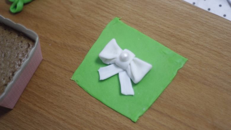 零基础纸杯翻糖蛋糕,带子沾点水贴在蝴蝶结底部，“结”上面再加一个大号的装饰珍珠糖。