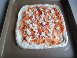玉米培根披萨,在披萨面团坯上涂上一层番茄酱，洒上一半的芝士碎