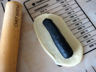 豹纹吐司,接着包白色的面团，这次的白色面团需要擀宽长一些，能把竹炭的完全包起来，接缝处捏紧。
