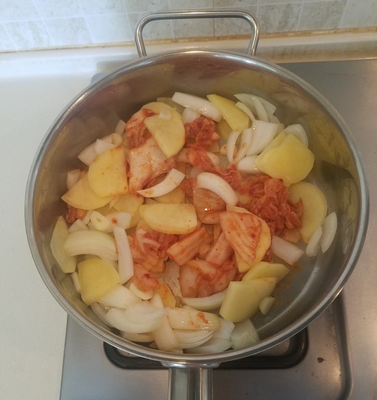 泡菜锅,炒至土豆和元葱变软后加入辣白菜继续翻炒。