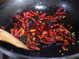 干煸孜然花菜,接着放入干红辣椒段、姜片、蒜片炒出香味。