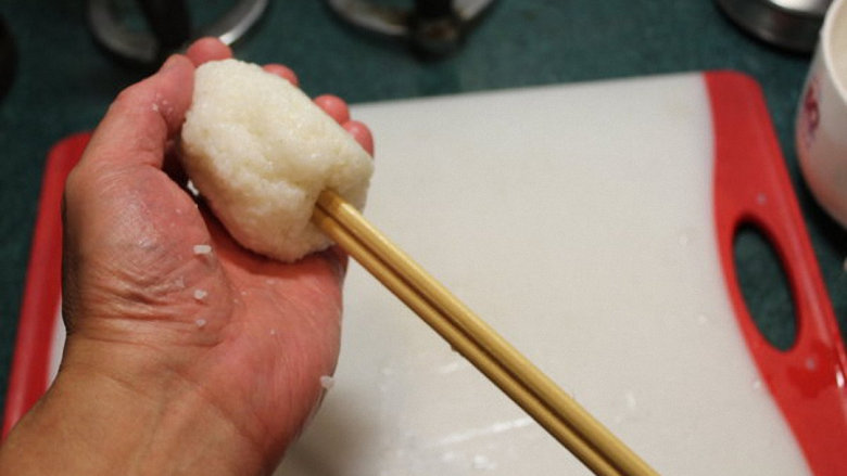 烤米卷,准备一杯盐水，将手沾湿后，取适当大小捣好尚热的米饭，揉成圆饭团，将竹棍或竹筷插入饭团。