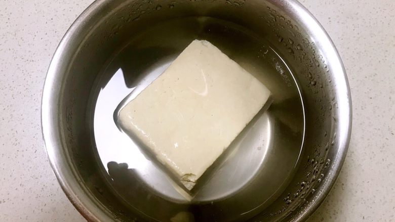 红油豆瓣烧豆腐,把豆腐浸泡在冷水中，加入1勺精盐，浸泡60分钟，这样可以使豆腐更瓷实，不容易碎掉