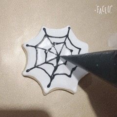 万圣节“捣鬼”糖霜饼干,表面晾干，用黑色糖霜来织出蜘蛛的网，