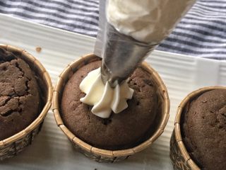 家有烤箱＋快手的巧克力杯子蛋糕,将奶油放入裱花袋，涂在蛋糕上，用抹刀抹平
