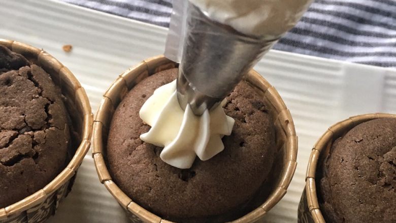 家有烤箱＋快手的巧克力杯子蛋糕,将奶油放入裱花袋，涂在蛋糕上，用抹刀抹平
