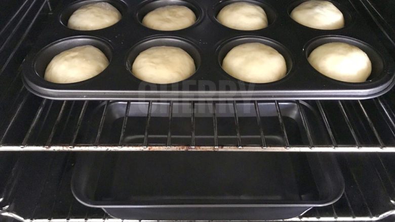#家有烤箱#黑芝麻豆沙面包,将包好的面团，倒扣在马芬蛋糕的磨具中，放入有温度的烤箱中层，下层装一盒开水，进行第二次发酵。