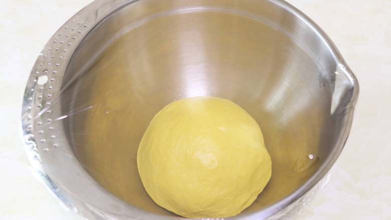 南瓜肉松芝麻包,将面团取出，放入一个干净的容器中，盖上保鲜膜，进行基础发酵1小时