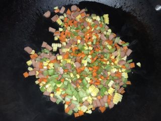 五宝炒饭,油锅里放入玉米、胡萝卜、芹菜、鸡肉肠翻炒，炒至材料断生