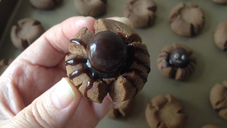蜘蛛可可饼干,先用牙签蘸点碟中的巧克力酱，在饼干两侧勾画出蜘蛛的8条腿，再把黑巧克力豆放在上面