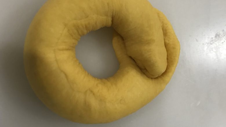 南瓜圈圈面包,卷起来，另一头放在压扁的面团上，用压扁的面团包好并收口。