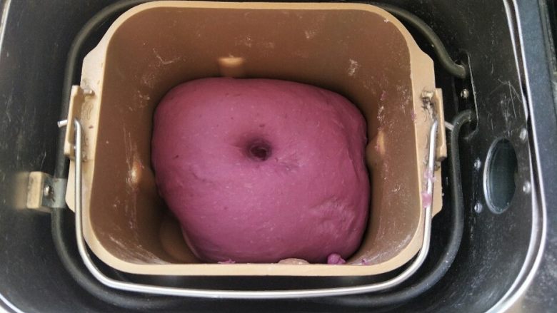 紫薯面包,将面团从面包机里拿出来，然后把面团整圆，放回面包桶里发酵，时间设置一个小时。面团发酵两倍大，手指粘面粉戳洞，洞口不会缩不塌陷，面团即发酵完成。