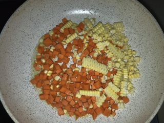 三文鱼三色蔬炒饭,另一个不粘锅加入油，放入胡萝卜丁和玉米粒，摊开后盖盖1-2分钟，直到胡萝卜变软。