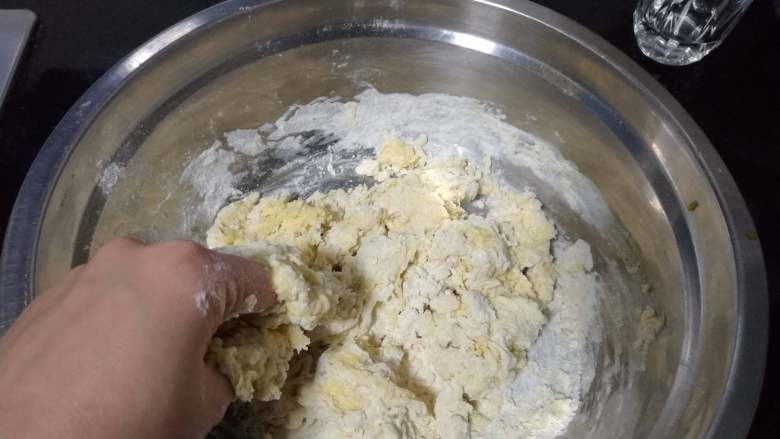 面包入门基本功之黄油面包卷,蛋液倒入面盆，用手指捏至没有明显干粉。期间可以视情添加调整用的20克水。
