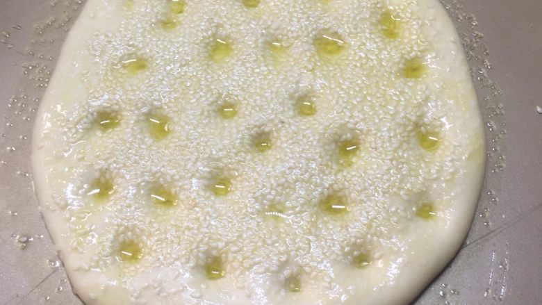 白芝麻佛卡夏,用手指关节在发酵好的面包胚上按上小孔。均匀的刷上橄榄油，多刷点。撒上薄盐。