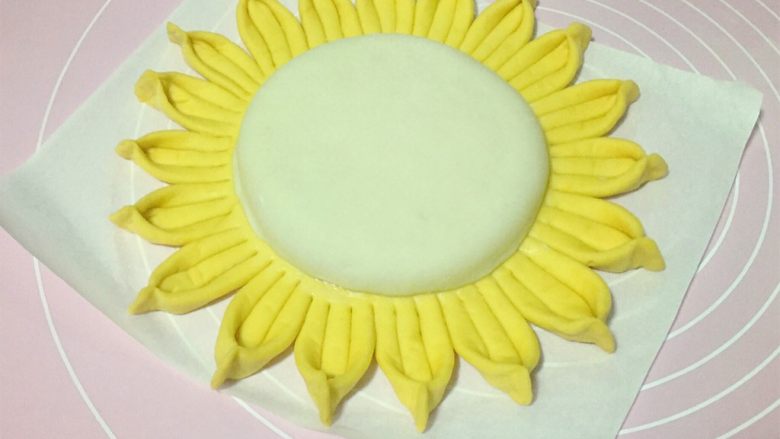 吃掉一朵花+向日葵花馒头,再取白色面剂子擀成小圆饼，先在黄面饼中间圆形的地方刷一层水，然后把擀好的白面饼放在黄面饼中间。