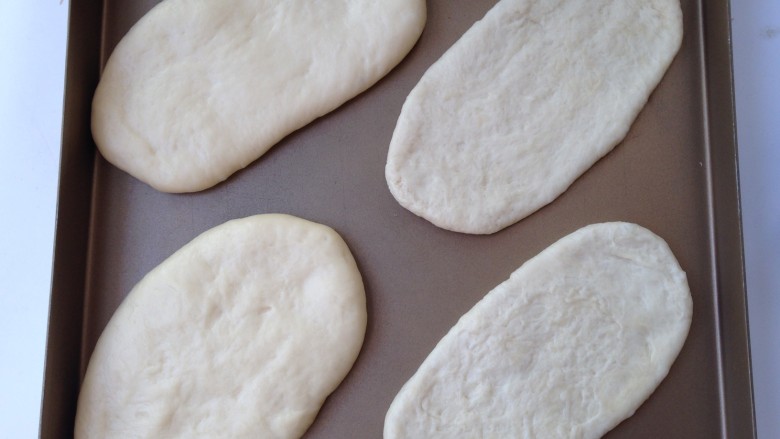 香葱培根面包,面团移至揉面垫上排气后，分为等量的四份，擀成牛舌椭圆状摆入烤盘，放入烤箱开启发酵功能进行二发