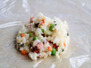 杂蔬丸子饭团,砧板上铺上一层保鲜膜，放入一勺炒好的米饭；