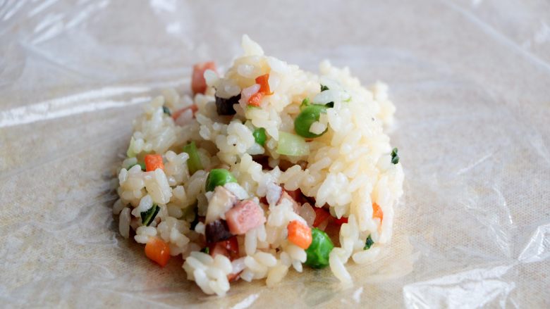 杂蔬丸子饭团,砧板上铺上一层保鲜膜，放入一勺炒好的米饭；