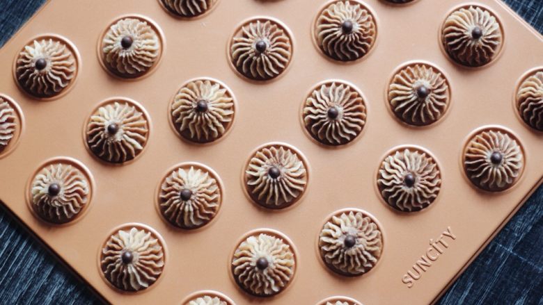 巧克力双色曲奇,裱花袋垂直均匀用力挤在阳晨马卡龙烤盘里，上面放一颗耐烘焙巧克力豆。