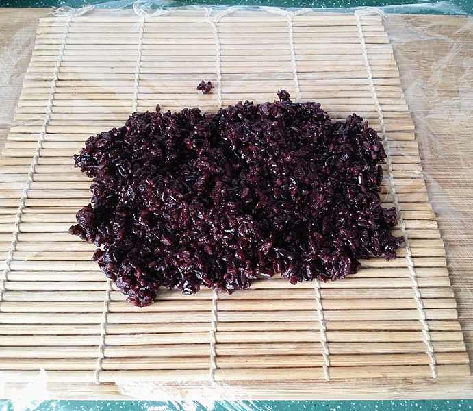双糯米蒸饭包油条,在寿司帘上铺张保鲜膜、放上适量黑糯米饭