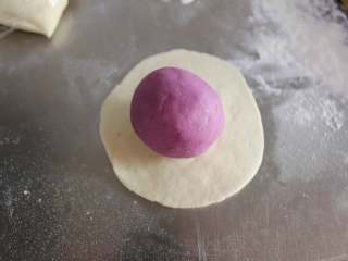 开花紫薯馒头,白色的擀成小圆片，紫色的用手团成面团，如图中这个样子，紫色的面团光滑的部分朝下，白色的包住紫色的面团收口捏紧，成一个白面团的形状。