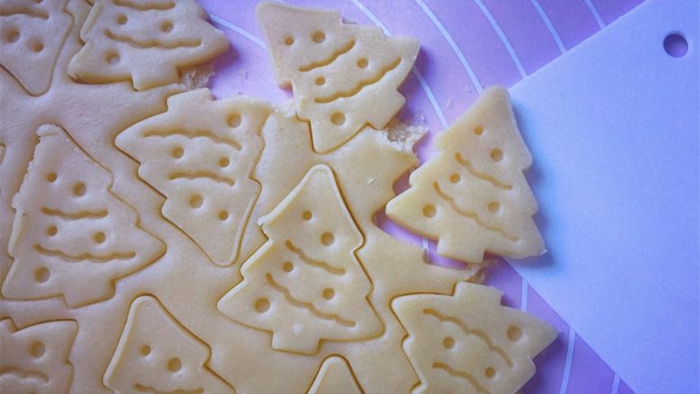 圣诞树饼干,小心去掉周边的面片，（去掉的面片还可以重复擀开使用）然后用刮刀移铲到不粘烤盘上。